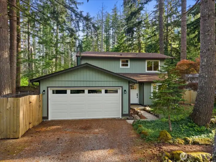 Front Exterior – Two-story home with attached two-car garage, updated exterior finishes, and a welcoming entry path. Mature trees and natural landscaping create a private wooded setting.