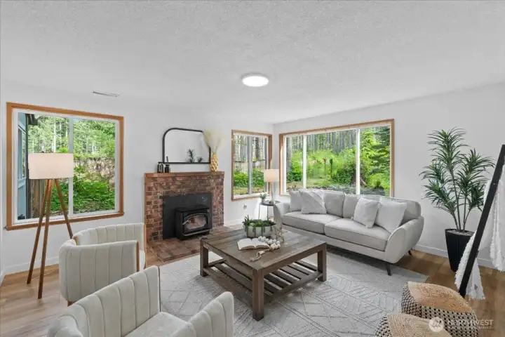 Living Room – Comfortable gathering space with brick fireplace, large picture windows, and abundant natural light. Views of the surrounding greenery create a relaxing atmosphere.