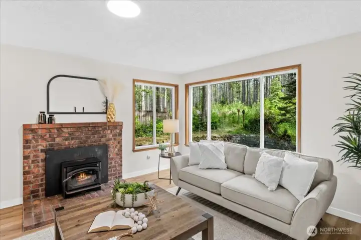 Living Room – Spacious living room featuring a brick fireplace, oversized windows, and peaceful backyard views. Natural light enhances the warm and comfortable atmosphere.