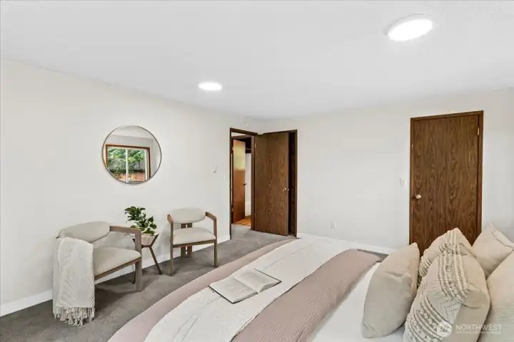 Primary Bedroom – Spacious bedroom with neutral décor, seating area, and large windows overlooking mature trees. Comfortable layout provides both sleeping and relaxation space.