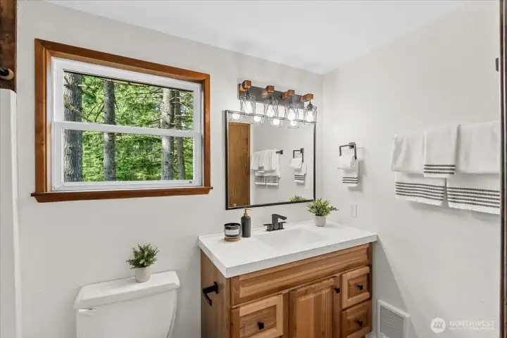 Bathroom – Updated bathroom featuring a modern vanity with solid-surface countertop, contemporary lighting, and a large window providing natural light and treed views.