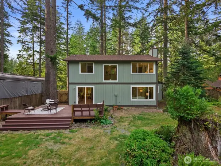 Rear Exterior – Back of the home featuring a spacious deck, fenced yard, and mature landscaping surrounded by towering trees.