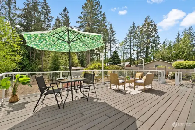 An immense composite deck with glass railing overlooks a private backyard where towering evergreens provide a natural backdrop.This deck is an entertainers dream with room to create a beautiful yet comfortable outdoor living area.