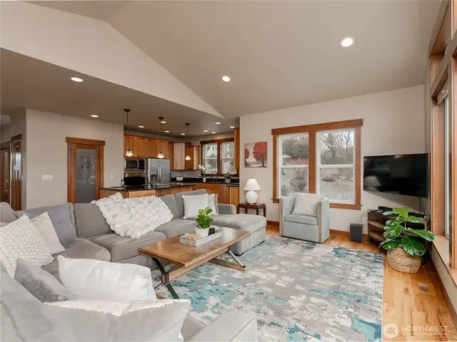 View of living room looking towards kitchen w/ vaulted ceilings, hardwood floors and oversized windows.