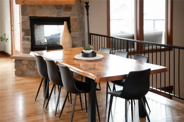 View of dining room w/ double sided stone fireplace, oversized windows and French doors leading out to the main level lake view deck and outdoor living area.