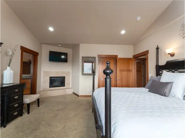 View of the spacious main level Primary Bedroom Suite w/ French doors leading to the lake view deck and outdoor living area, complete w/ fireplace and walk-in closet.