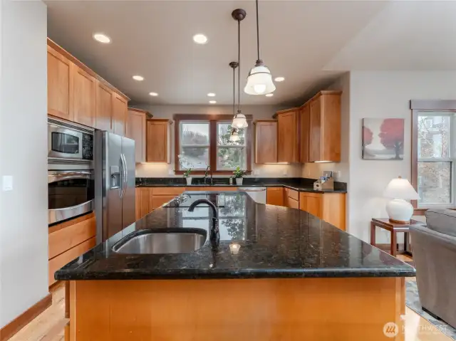 View of main level entertainer's kitchen w/ custom wood cabinetry, stainless steel appliances, granite countertops, and large island w/ bonus prep sink.