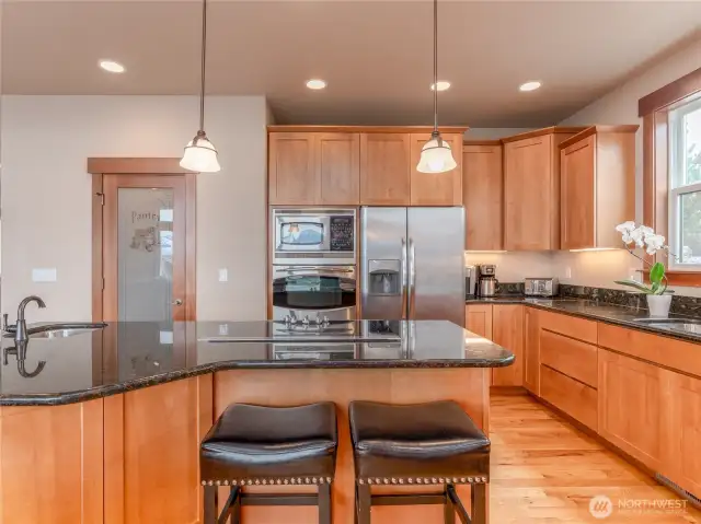 View of entertainer's kitchen with custom wood cabinetry, walk-in pantry, stainless steel appliances, granite countertops, oversized island, bonus prep sink and sit up bar.