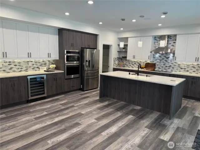 This view features the Stunning Dry Bar Slab Quartz Counter, Beautiful Cabinets with Wine Fridge and Appliance wall with Gleaming Stainless Steel Wall Oven, Microwave and Refrigerator. Large Walk-in Pantry in the corner.