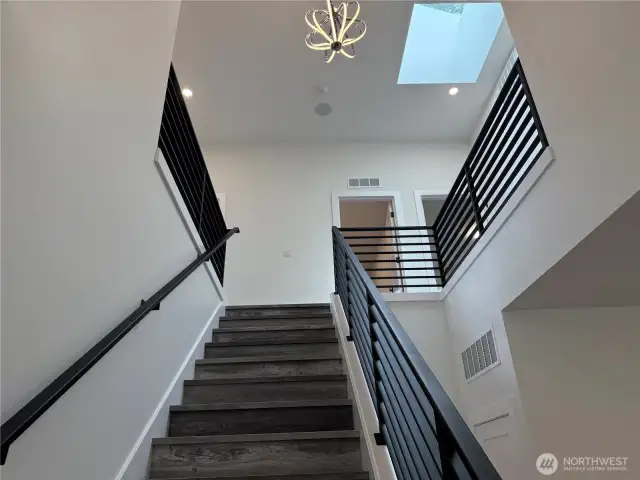 Dramatic Vaulted Ceiling with Skylight and Gorgeous Modern Chandelier. Look how Beautiful the Staircase is with the Planked Stairs and Modern Black Coated Metal Hand Railing too.