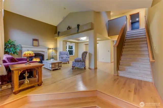 Step through the inviting entry into a stunning living room featuring rich hardwood floors, soaring vaulted ceilings, and a cozy gas fireplace.