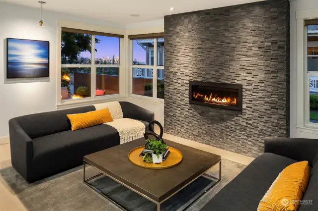 Living room with floor to ceiling tiled fireplace and views of downtown Seattle.  Built in sound system and gallery lighting.  Tons of light.  Designer shades.  Living room connected with kitchen and dining spaces for entertaining.