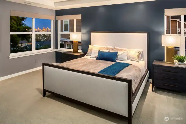 Spacious primary bedroom with views of downtown Seattle and gorgeous trees.  Recessed, high-ceilings give this room an expansive feel.  Just steps to the en suite bath of your dreams!