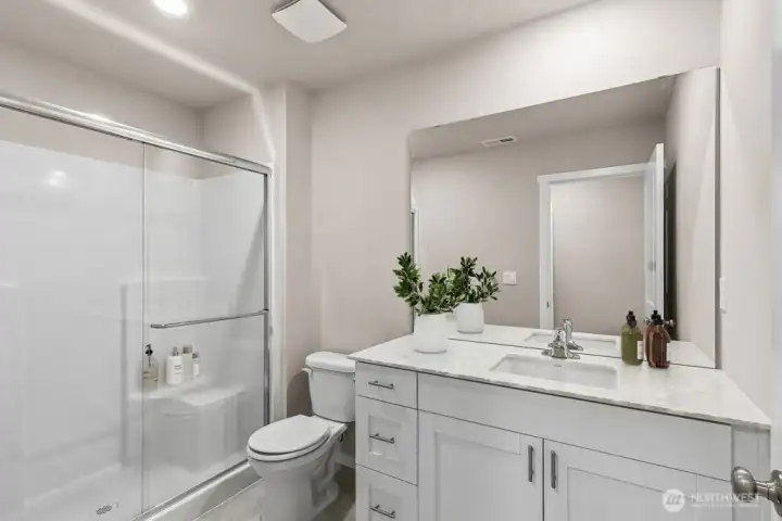 En-suite bath pairs a sleek quartz vanity and under-mount sink with a glass-enclosed shower and built-in seat for easy upkeep. Pictures are for representational purposes only, colors and features may vary