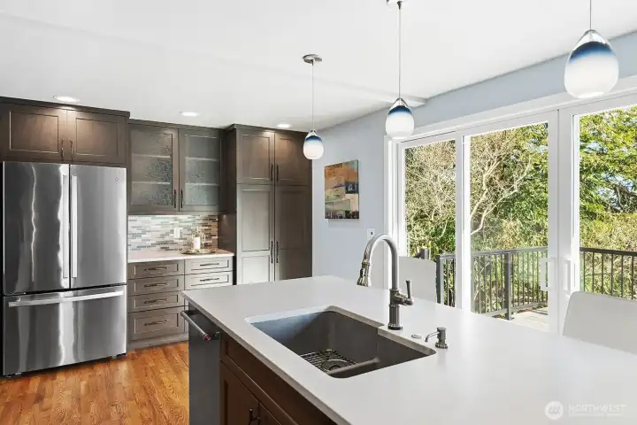 Glass front cabinets, a bar area for coffee or beverages, pantry and fridge on the North wall of the kitchen. Lovely pendant lighting over the island and a great outlook to the back yard enhance the space.