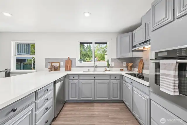 Newly refreshed kitchen with quartz countertops, tile backsplash, sink, refrigerator, and cooktop.