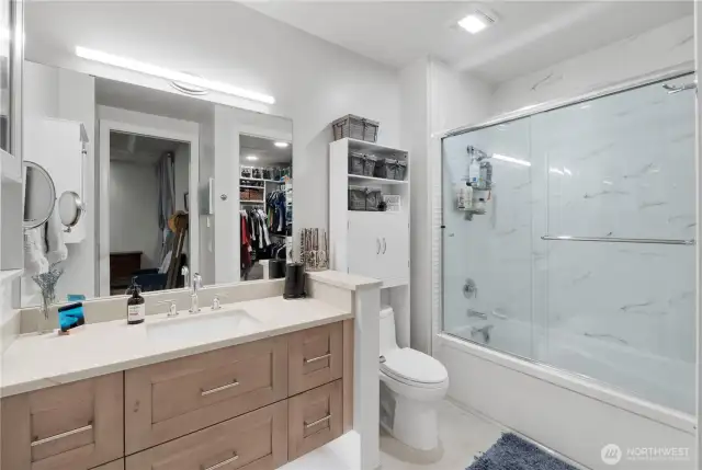 Where form meets function.  This full bathroom blends modern elegance with practical comfort. A quartz-topped vanity with soft-close drawers offers ample storage, while the oversized mirror and sleek lighting make the space feel bright and open. The layout smartly connects directly to the walk-in closet, creating a private dressing suite feel. Everything you need, right where you want it.