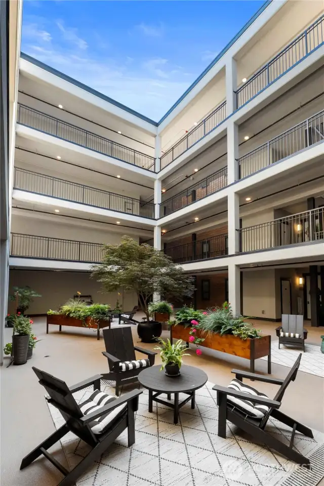 At the heart of the Rainier Building, this open-air community atrium offers a peaceful retreat just steps from your front door. Designed for both social gatherings and quiet moments, the space features modern Adirondack seating, patterned outdoor rugs, raised garden beds, and lush greenery throughout. Whether you’re sipping coffee in the morning light or enjoying an evening conversation with neighbors, this thoughtfully curated courtyard feels more like a private garden than a condominium common area. Covered and protected from the elements, it provides year-round usability and adds a distinctive touch of calm to daily life.