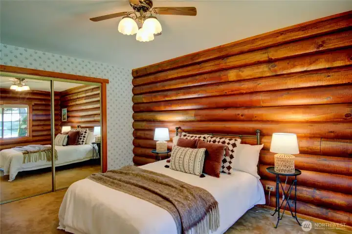 Primary bedroom featuring mirrored closet doors and a log wall that creates a striking headboard backdrop.