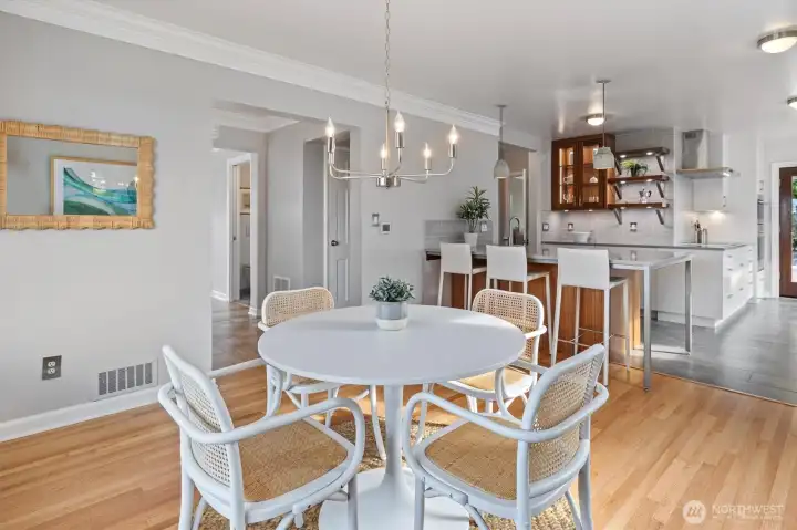 Light-filled dining area with refinished hardwood floors and crisp crown moulding flows seamlessly into the updated kitchen. Modern pendant lighting, a sleek chandelier, and open sightlines create the perfect setting for everyday meals and entertaining.