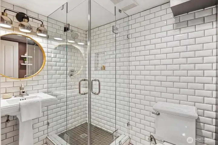 Stylish lower-level ¾ bath with frameless glass shower, subway tile surround, pedestal sink, and modern lighting—fresh, functional, and thoughtfully designed.
