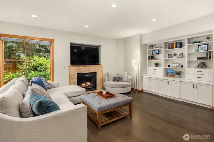 White Oak hardwood floors flow throughout the main level into a spacious family room with one of two fireplaces with travertine tile surround, built-in bookcases, cabinets and views to the outdoor space.