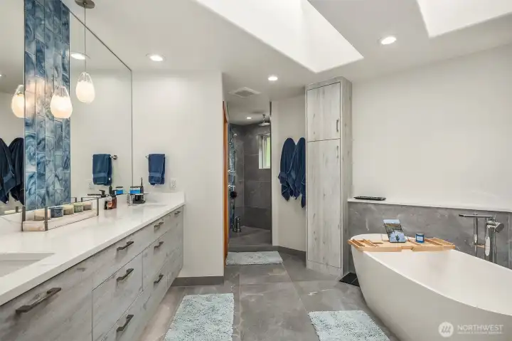 A lavish, stunning, 5-piece en suite bath boasting heated floors, soaking tub, floating dual vanity, large pass-through shower with rain head, bench, and beautiful tilework, fixtures & lighting.