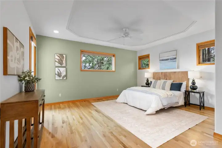 Light pours into the primary bedroom with hardwood floors and tall ceilings.
