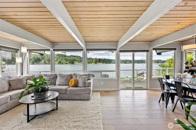 Let the lake greet you every morning. This bright, open living space is wrapped in glass, offering unobstructed views of the shimmering water just beyond. Soft natural light and a warm wood-plank ceiling invite slow mornings and golden-hour gatherings.