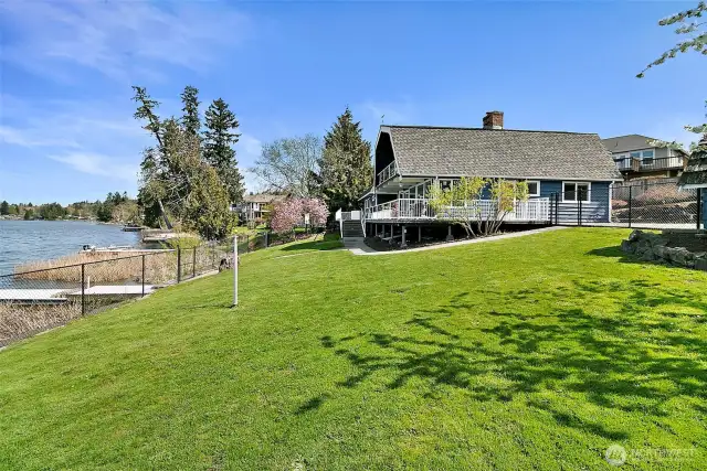 Lakeside Lawn and Home View – A wide grassy lawn slopes gently toward the water, offering an expansive view of this stunning property.