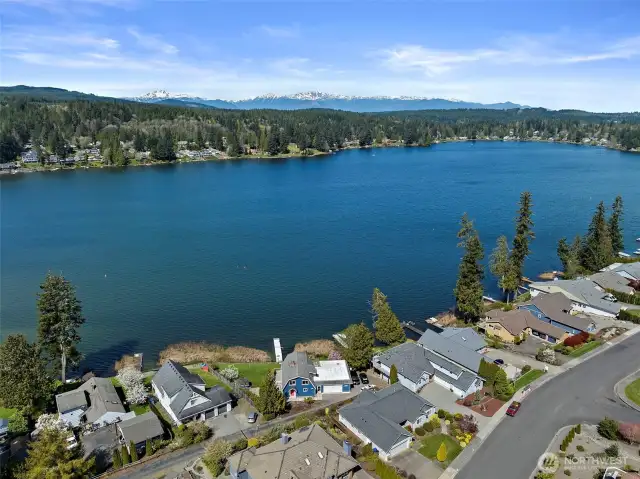 A majestic view from above the lake, revealing forested surroundings and the Olympic Mountains in the distance.