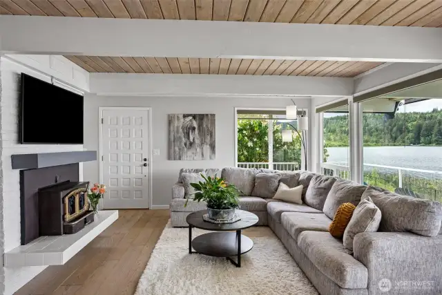 This beautifully designed living room blends cozy warmth and scenic beauty with a wood-burning fireplace, natural wood ceilings, and expansive lake views—perfect for curling up in any season.