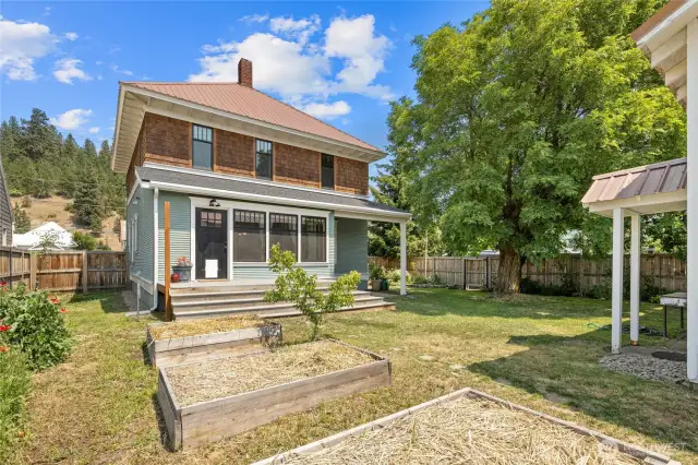 The backyard with raised garden beds and large oak tree creates an outdoor retreat.