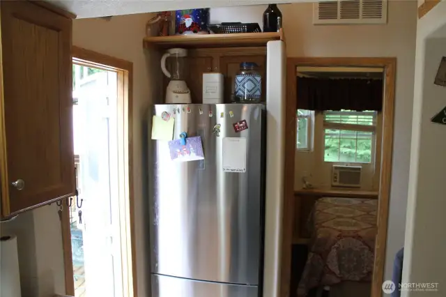 This view is of the refrigerator side of the kitchen and the bedroom behind it.