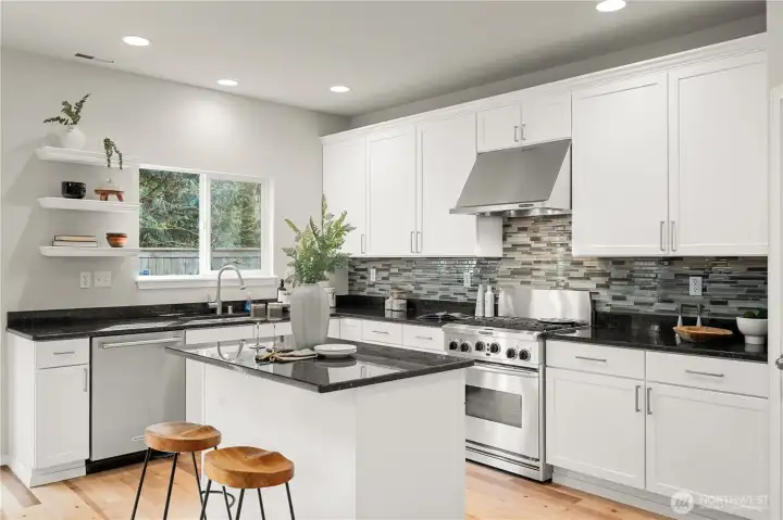 A beautifully appointed kitchen showcases crisp white cabinetry paired with a spacious center island, creating a bright and functional hub for everyday living and entertaining. Sleek black granite countertops provide striking contrast, complemented by the tile backsplash that adds texture and visual interest. The space is outfitted with stainless steel KitchenAid appliances. A walk-in pantry offers abundant storage, enhancing both convenience and organization in this thoughtfully designed kitchen.