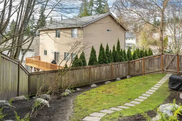A serene, grassy side yard offers a peaceful outdoor space. Surrounded by mature trees, lush ferns, and hosts, the space feels private and secluded, with a tranquil setting. This space in a unique aspect of this lot in the neighborhood. It's a great extension from the patio and provides opportunity for additional gardening.