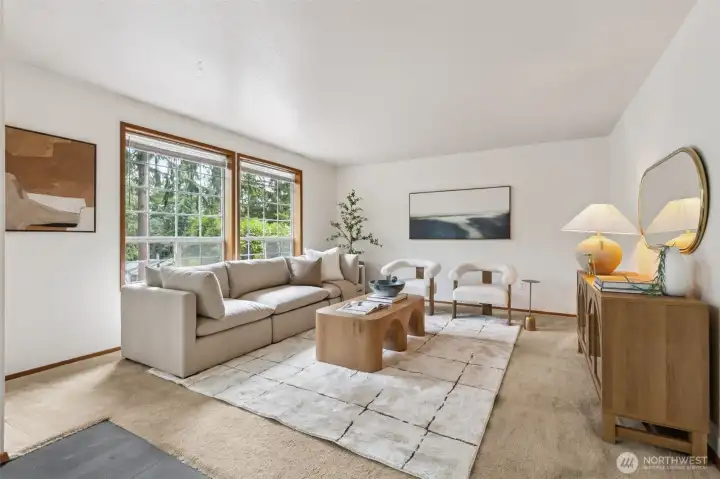 Bright and inviting living room featuring large picture windows with serene forest views, soft neutral décor, and an open, calming layout—perfect for relaxing or entertaining.