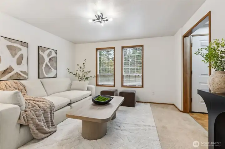 Bright and welcoming sitting room featuring large windows, neutral tones, and a comfortable, modern layout—perfect for gathering or unwinding.