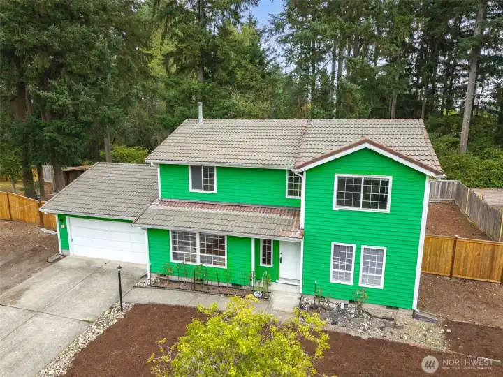 Front exterior of 513 Hidden Forest Dr SE in Olympia — a spacious two-story home tucked against a serene backdrop of mature evergreens. Features include an oversized driveway, two-car garage, fresh exterior paint, and a fully fenced side yard with wide gate access. Low-maintenance landscaping and a peaceful cul-de-sac setting create an inviting first impression. No HOA!