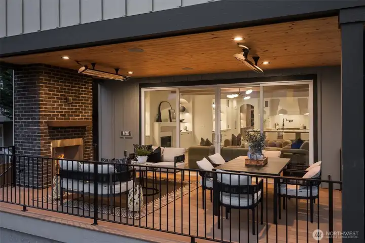 Covered outdoor living area featuring a cozy fireplace, heated pannels for all year round living and entertaining, ample space for dining and lounging, and Sonos speakers.