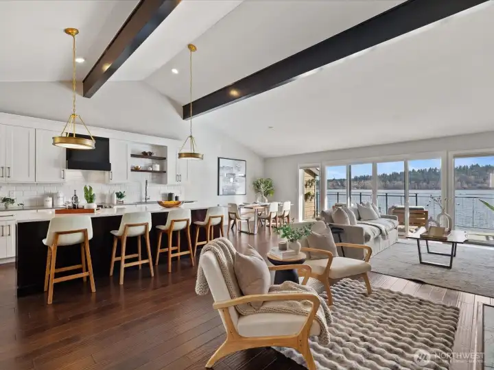 Open-concept living and kitchen area with island seating, vaulted ceilings, hardwood flooring, and access to waterfront deck