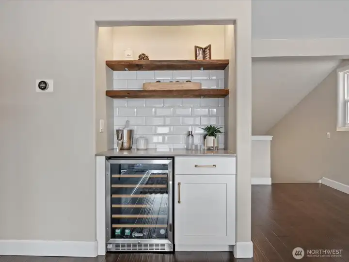 Built-in wet bar with beverage fridge, open shelving, tile backsplash, and countertop workspace