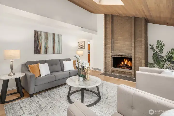 This architecturally distinctive living space showcases a beautiful brick fireplace beneath a vaulted wood-beamed ceiling, creating a warm and inviting atmosphere with genuine character. New flooring and fresh paint throughout elevate the space while honoring its unique mid-century inspired design.