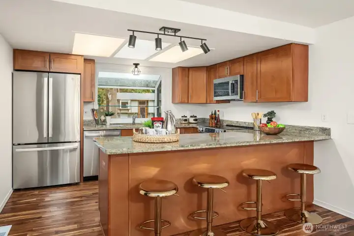 The updated kitchen features rich wood cabinetry, a breakfast bar with seating, and brand-new stainless steel appliances that deliver both style and functionality for the modern home chef. Sleek modern lighting and warm hardwood-style flooring tie the space together beautifully, creating a kitchen that is as inviting as it is practical.