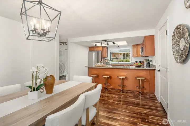 The dining area connects seamlessly to the kitchen, showcasing rich hardwood flooring, a modern chandelier, and warm sight lines into the updated kitchen beyond. This open and flowing layout is ideal for entertaining, creating a natural and inviting space where guests can gather comfortably from kitchen to table.