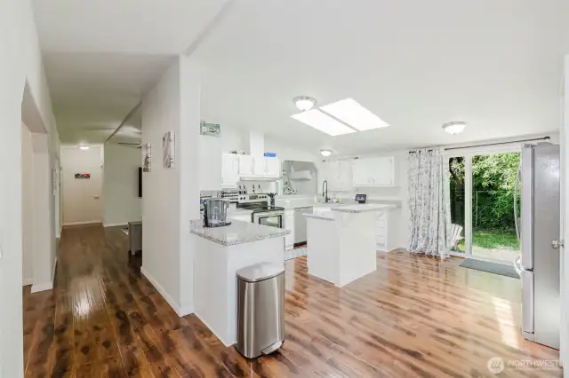 Look at that kitchen!! It's huge and beautiful! Dining room to the left. 1/2 bath for company down that hallway and the Primary bedroom is down there too!