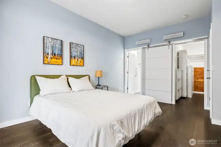 Now you see how it all connects. The flow is clean, direct, and exactly what you want in a primary suite. Straight ahead, the en suite bath is positioned for easy access, while the oversized walk-in closet sits right where it should. And that closet is not an afterthought. It’s framed with a crisp white sliding barn-style panel door that adds just enough architectural edge while keeping the footprint efficient. No swinging doors eating into your space here. It keeps the entire suite feeling open and well-orchestrated.