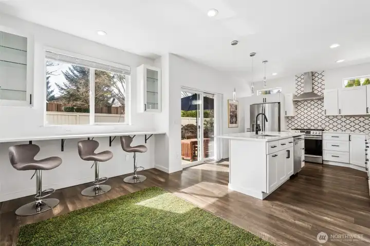 22. The window-lined bar stretches along the wall with bar chairs all included with the home, setting the scene for casual meals, coffee runs, or late-night chats that go longer than planned. The quartz island anchors the space with a touch faucet that feels just a little bit fancy and a stainless dishwasher tucked seamlessly below. The sliding glass door opens things up to the patio, giving you that easy back-and-forth flow when the doors are open and the weather’s cooperating. Overhead, three pendant lights hang with intention, fully dimmable so you control the mood at any hour. And those under cabinet outlets, quietly doing the most, keeping everything powered up and within reach without taking over the counters.