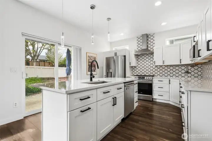 You’re looking straight across the island to that big sliding glass door, pulling in natural light and giving you an easy connection out to the patio. The matte black touch faucet is a little bit of a power move, sleek, modern, and just plain fun to use, paired with matching hardware on crisp white shaker cabinetry that keeps everything grounded and classic. And then there’s the backsplash, running all the way to the ceiling in a subtle Moroccan-inspired pattern that adds texture without overwhelming the space. Three low-profile pendant lights hover over the island, fully dimmable so you can shift the mood whenever you want. Stainless appliances are all included, and with the recent updates, this kitchen feels fresh.