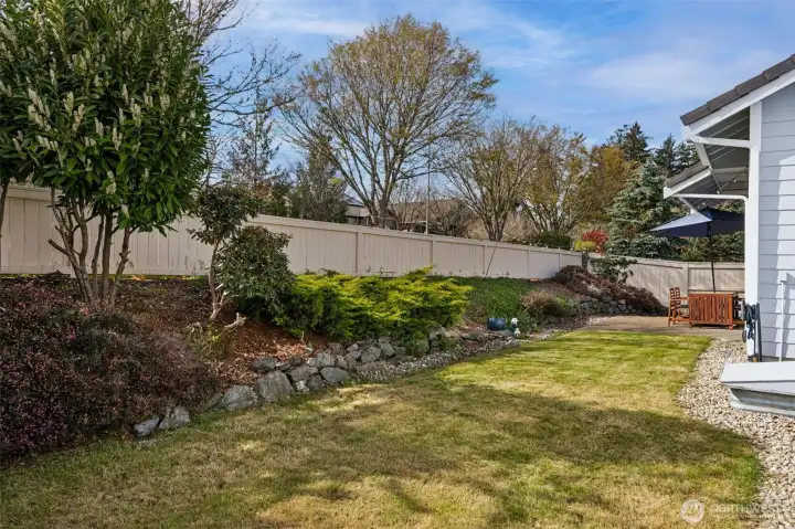 Along the fence line, you’ve got mature, low-maintenance landscaping that adds texture and greenery without signing you up for endless yard work. It frames the space beautifully while leaving plenty of open lawn to actually enjoy. And then along the home, that clean gravel border keeps everything crisp and polished, no muddy edges, no overgrowth creeping in.